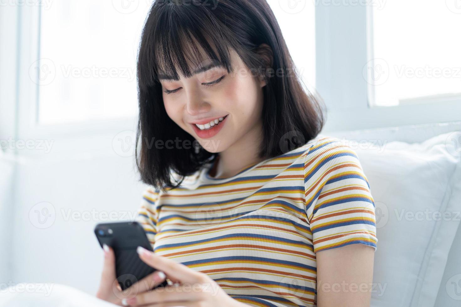 Hermosa mujer asiática con teléfono en la cama en el dormitorio foto