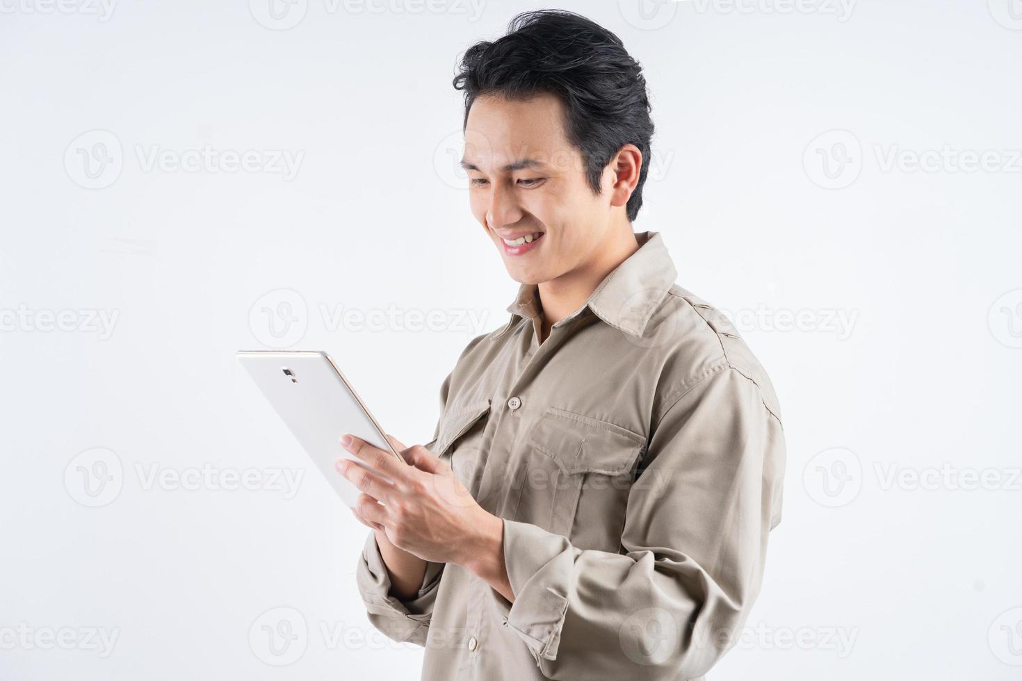 Apuesto joven mecánico en monos usando una tableta para trabajar y sonriendo foto