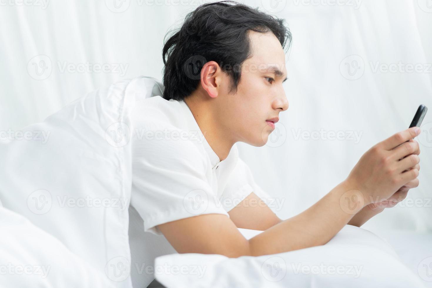 Young man lying in bed using a phone photo