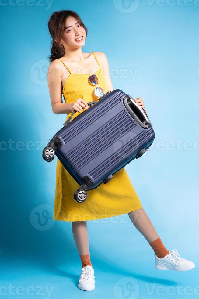 Joven mujer asiática sosteniendo la maleta sobre fondo azul, concepto de verano foto