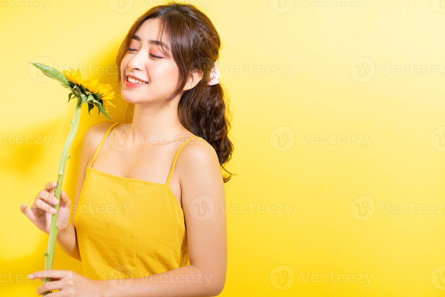 Hermosa mujer asiática sosteniendo y posando con girasol sobre fondo amarillo foto