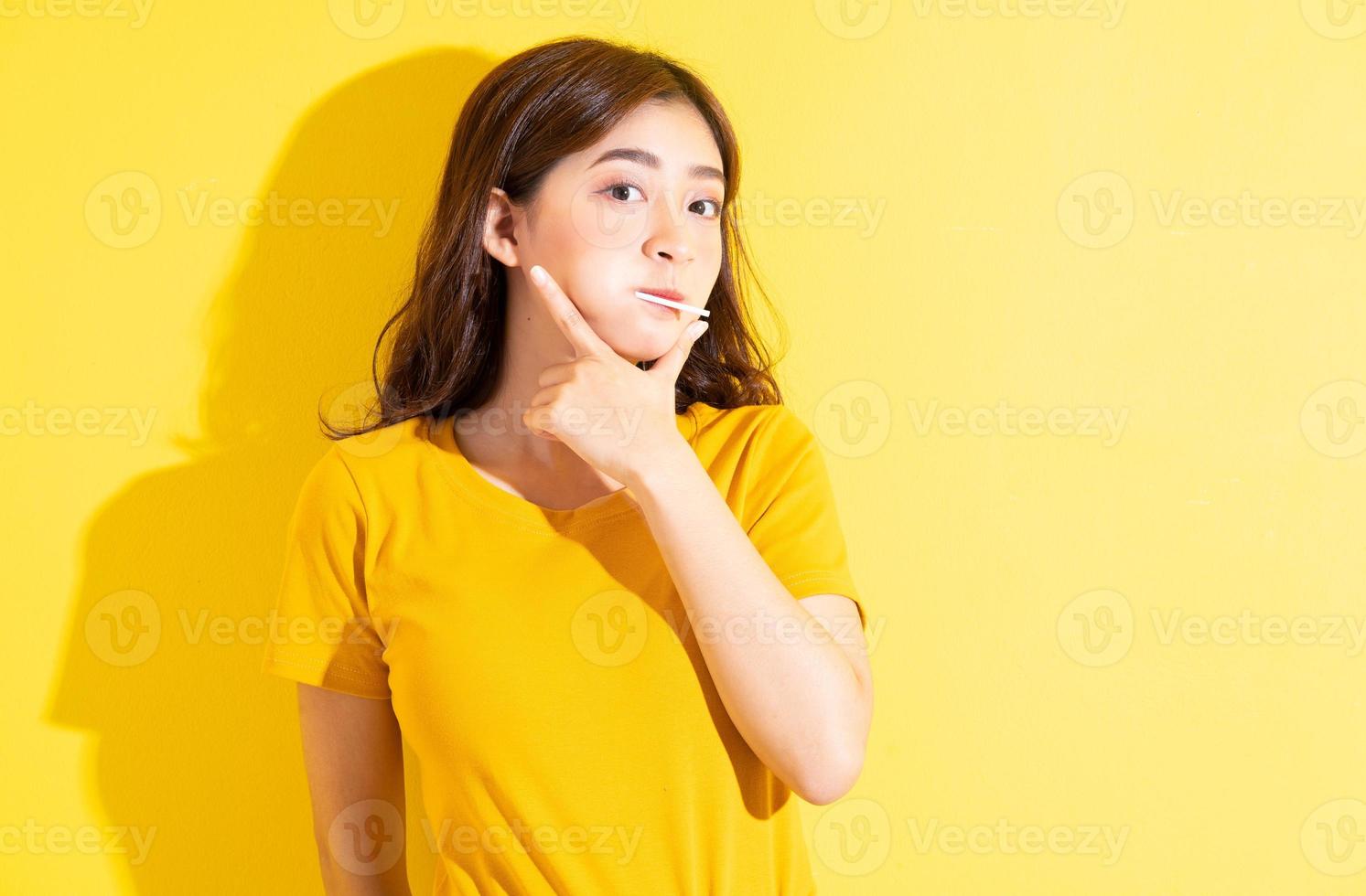 Joven mujer asiática comiendo piruletas sobre fondo amarillo foto