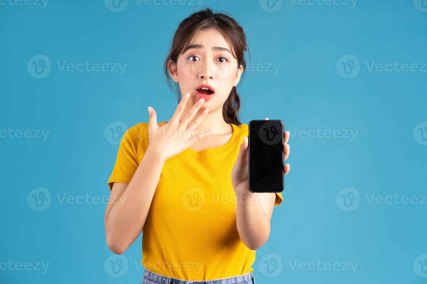 Joven mujer asiática de pie y con smartphone sobre fondo azul. foto