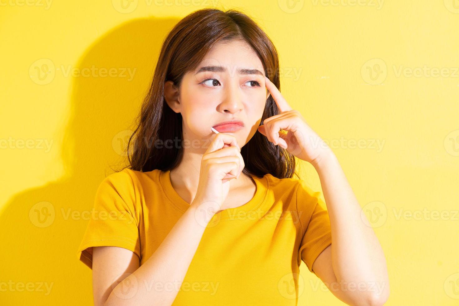 Joven mujer asiática comiendo piruletas sobre fondo amarillo foto