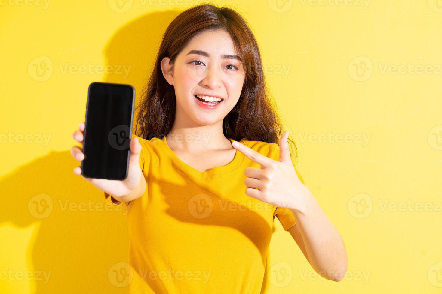 Joven asiática uisng smartphone sobre fondo amarillo foto