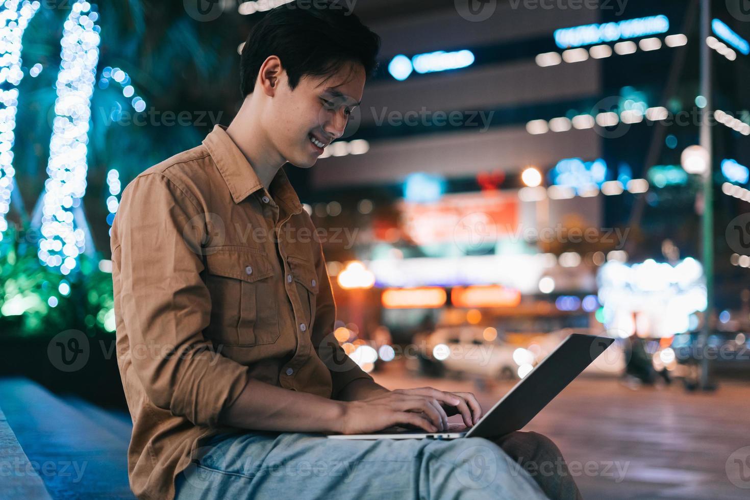 Joven asiático usando sentado y usando la computadora portátil en la calle foto