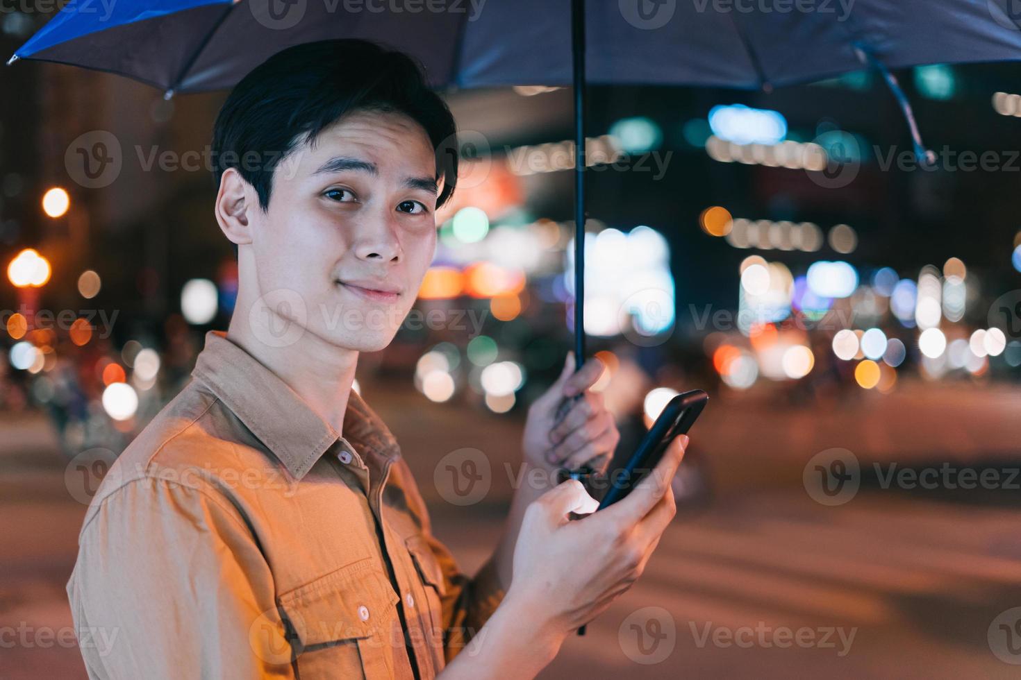 Joven asiático está usando su teléfono mientras camina en la calle por la noche foto