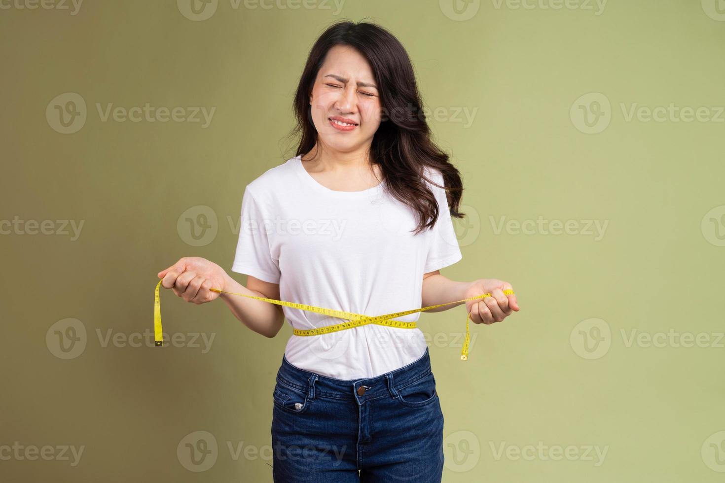 Joven asiática sosteniendo una cinta métrica molesta por el aumento de peso foto