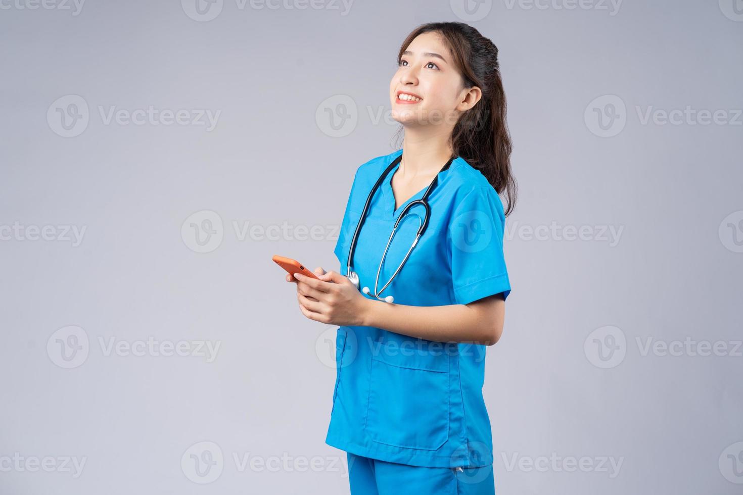 Young Asian doctor with smartphone on grey background photo