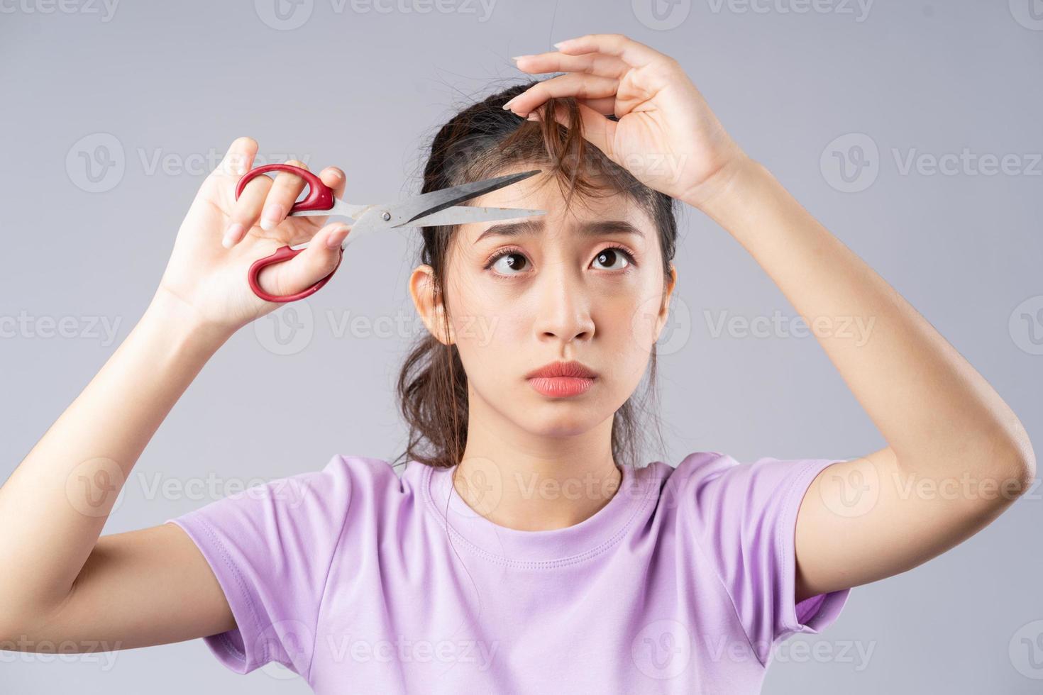 The young Asian girl was cutting her bangs with scissors photo