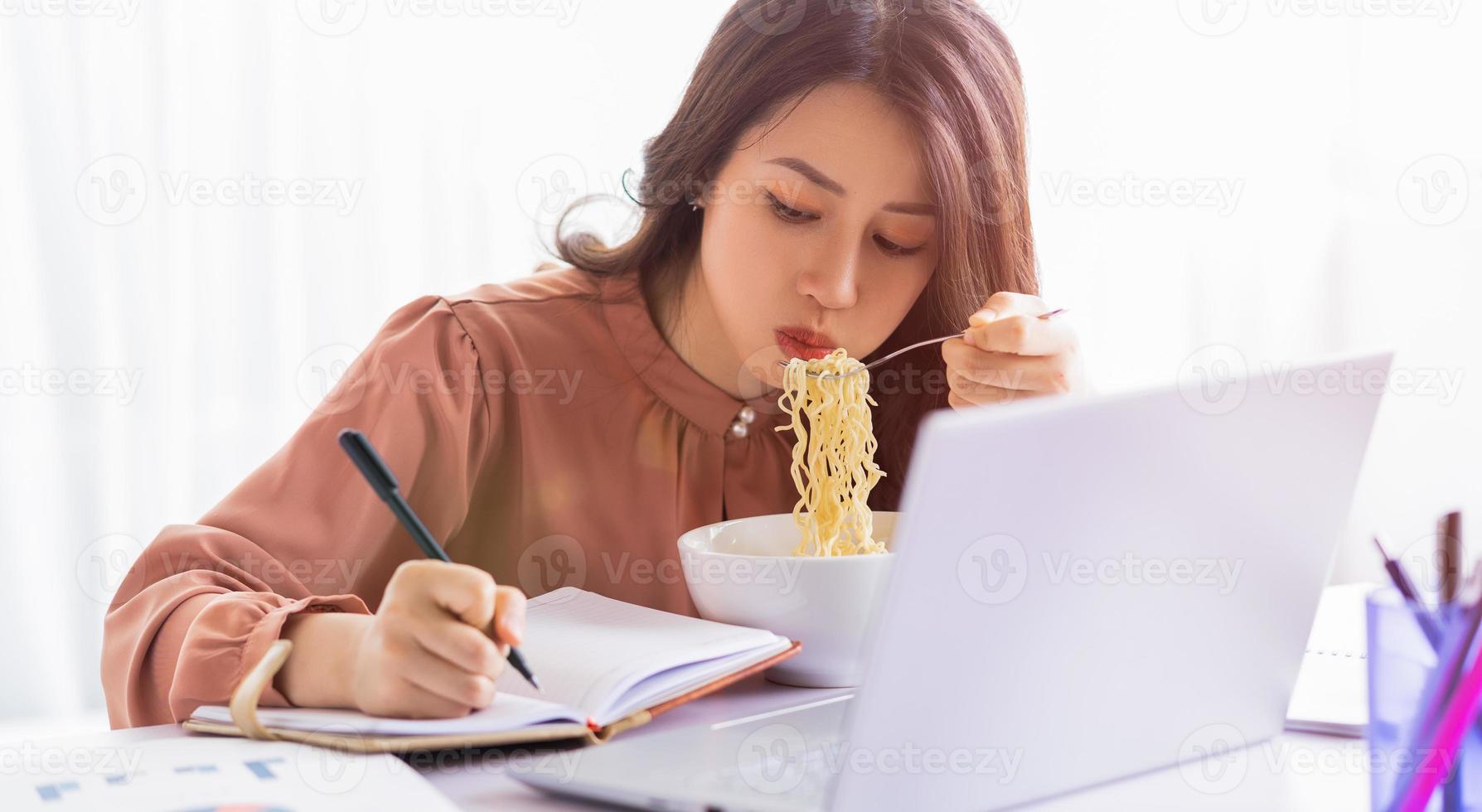 empresaria asiática tiene que comer fideos mientras trabaja foto