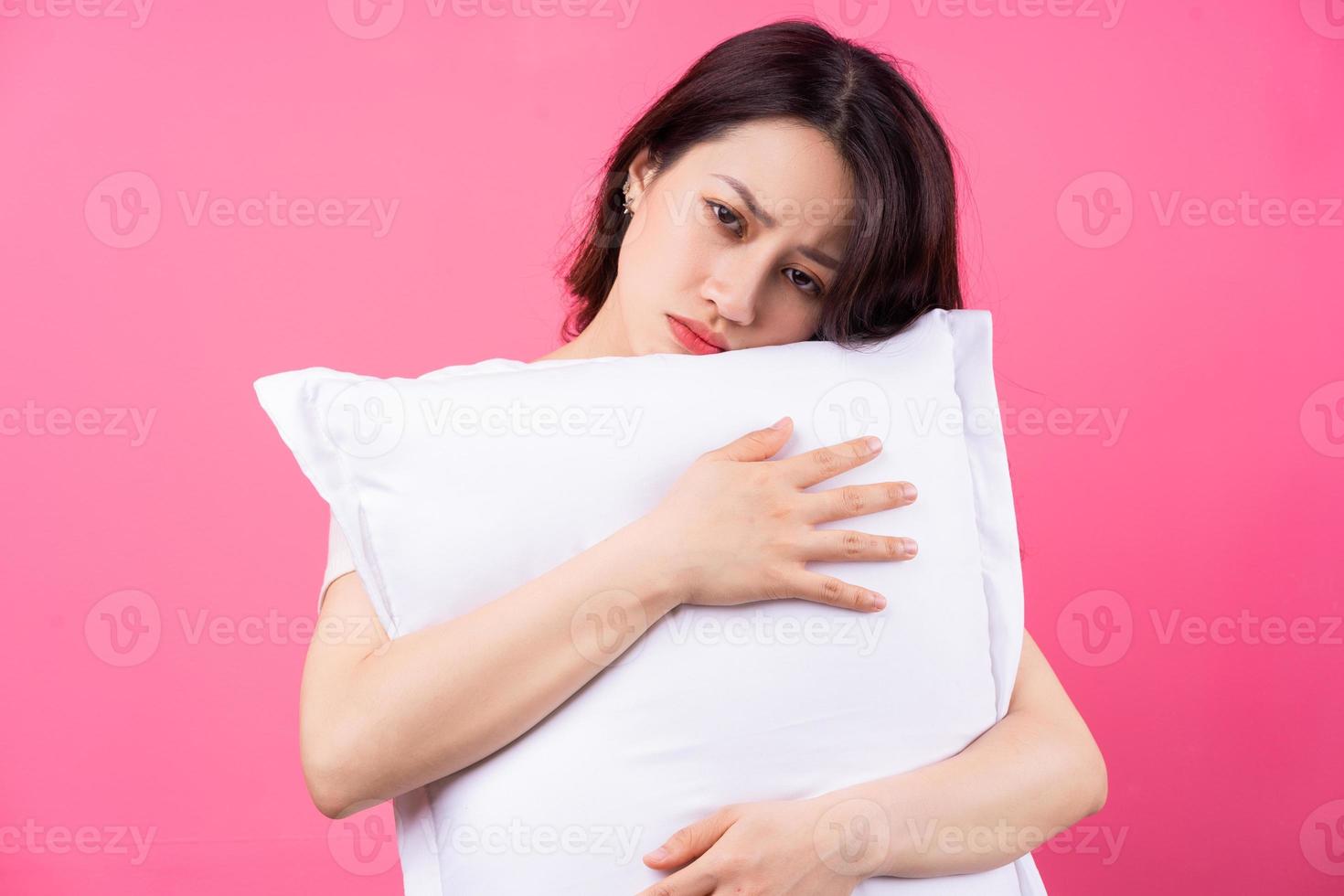 La mujer asiática está abrazando la almohada sobre fondo rosa foto