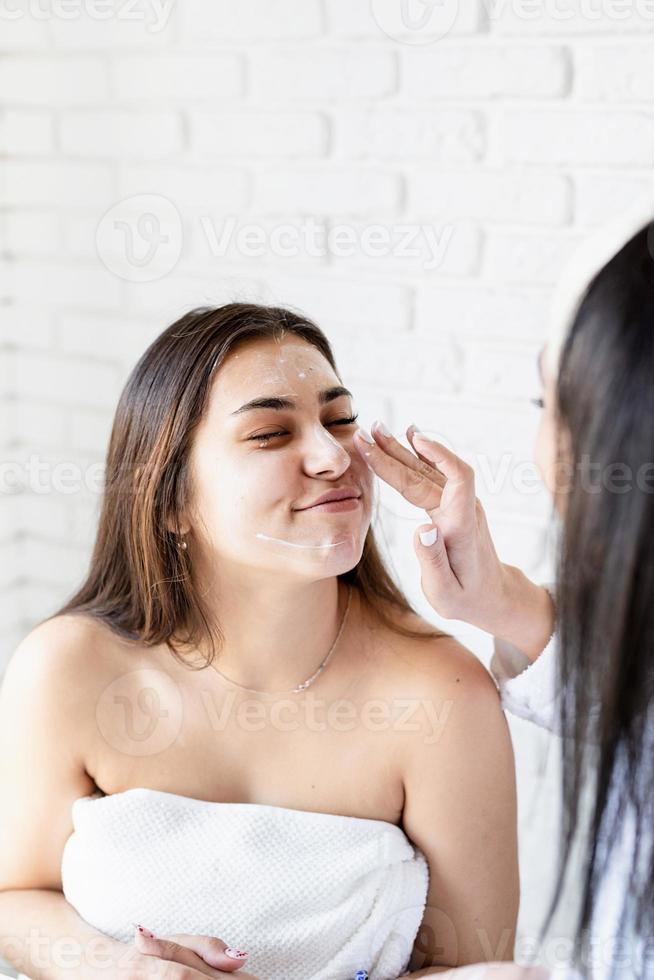 Dos hermosas mujeres aplicando crema facial haciendo procedimientos de spa foto