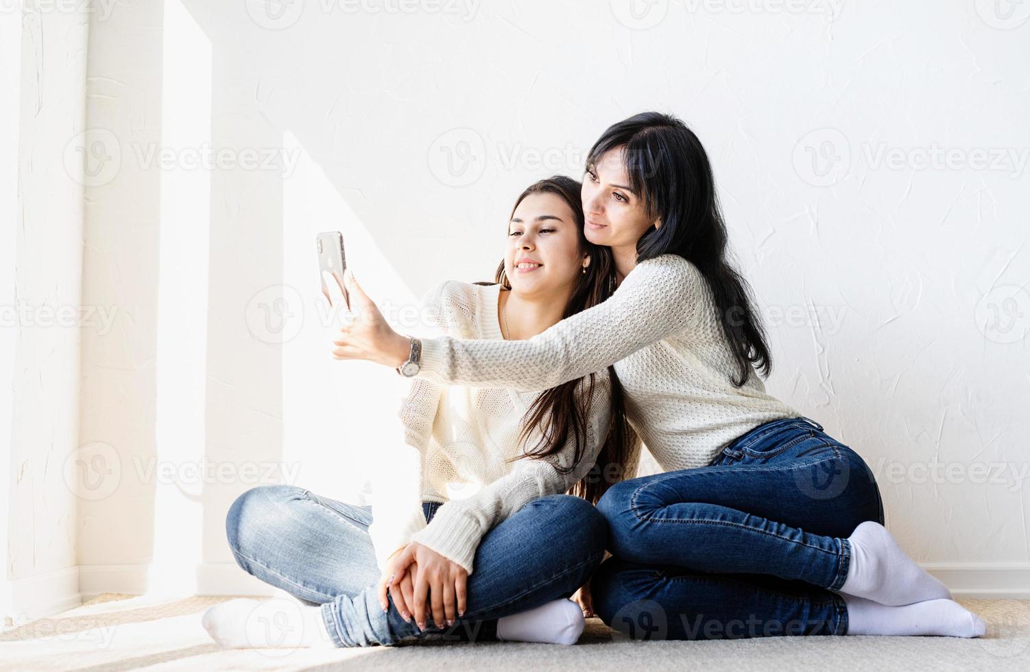 Two beautiful women taking selfie on mobile phone making funny faces photo
