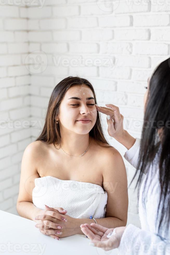 two beautiful women applying facial cream doing spa procedures photo
