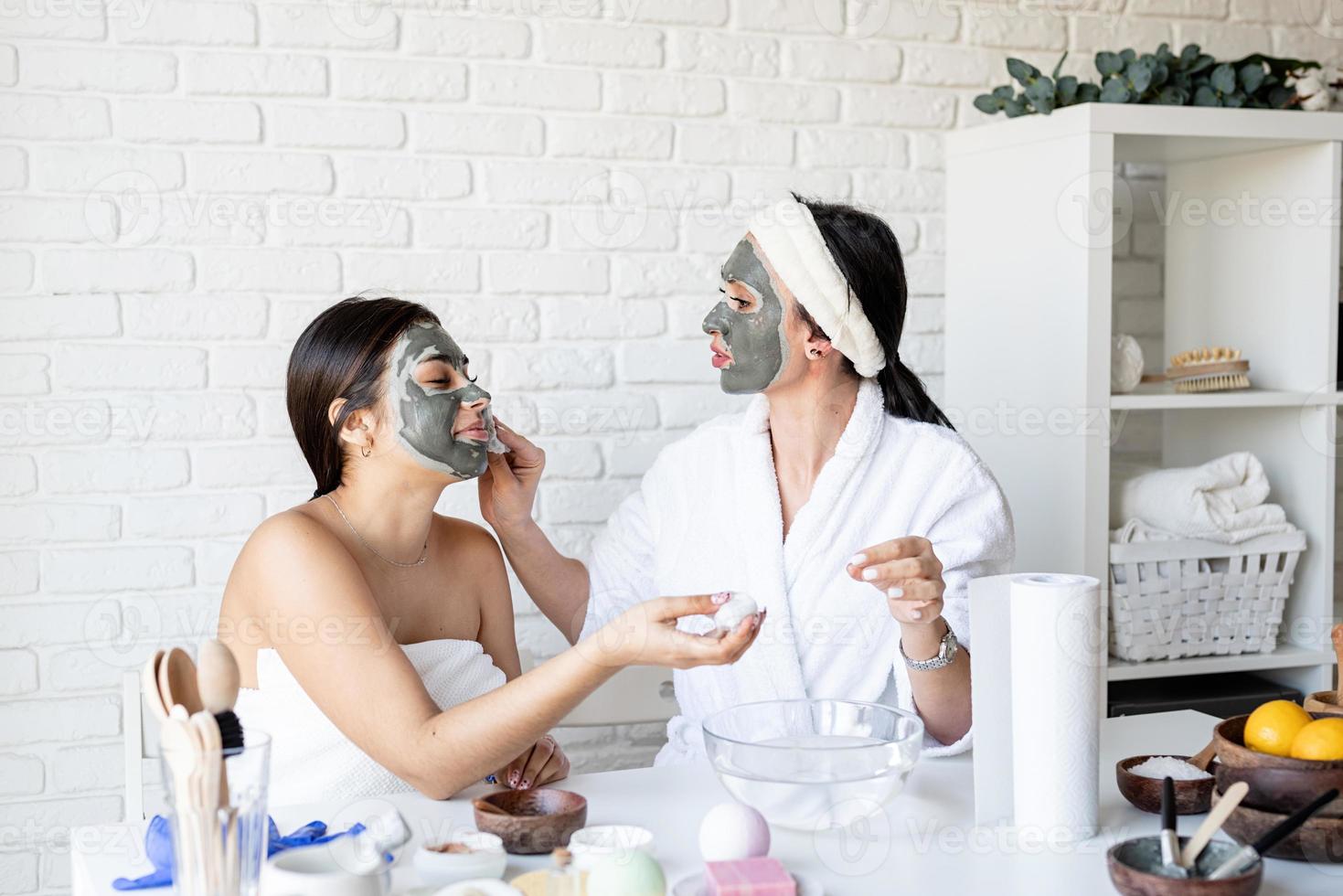 Dos hermosas mujeres aplicando mascarilla facial divirtiéndose foto