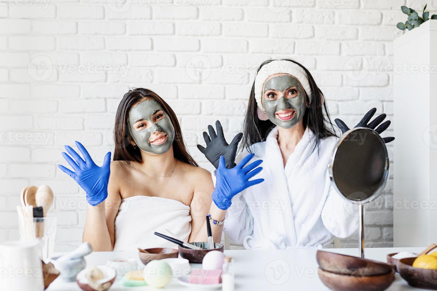 Dos hermosas mujeres en guantes aplicando mascarilla facial divirtiéndose foto