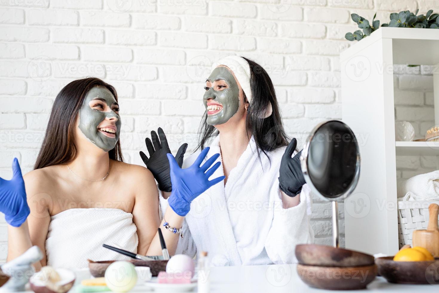 Dos hermosas mujeres en guantes aplicando mascarilla facial divirtiéndose foto