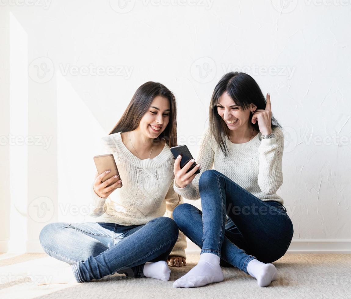 dos hermosas amigas enviando mensajes con teléfonos móviles foto