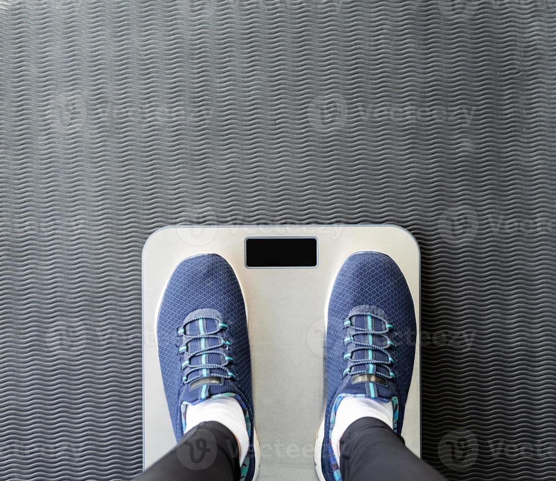 top view of female feet in blue sport shoes standing on scales photo
