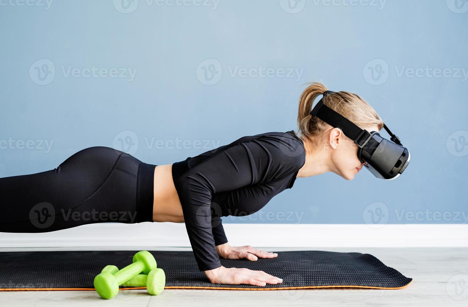 Joven mujer rubia con gafas de realidad virtual haciendo flexiones en casa foto