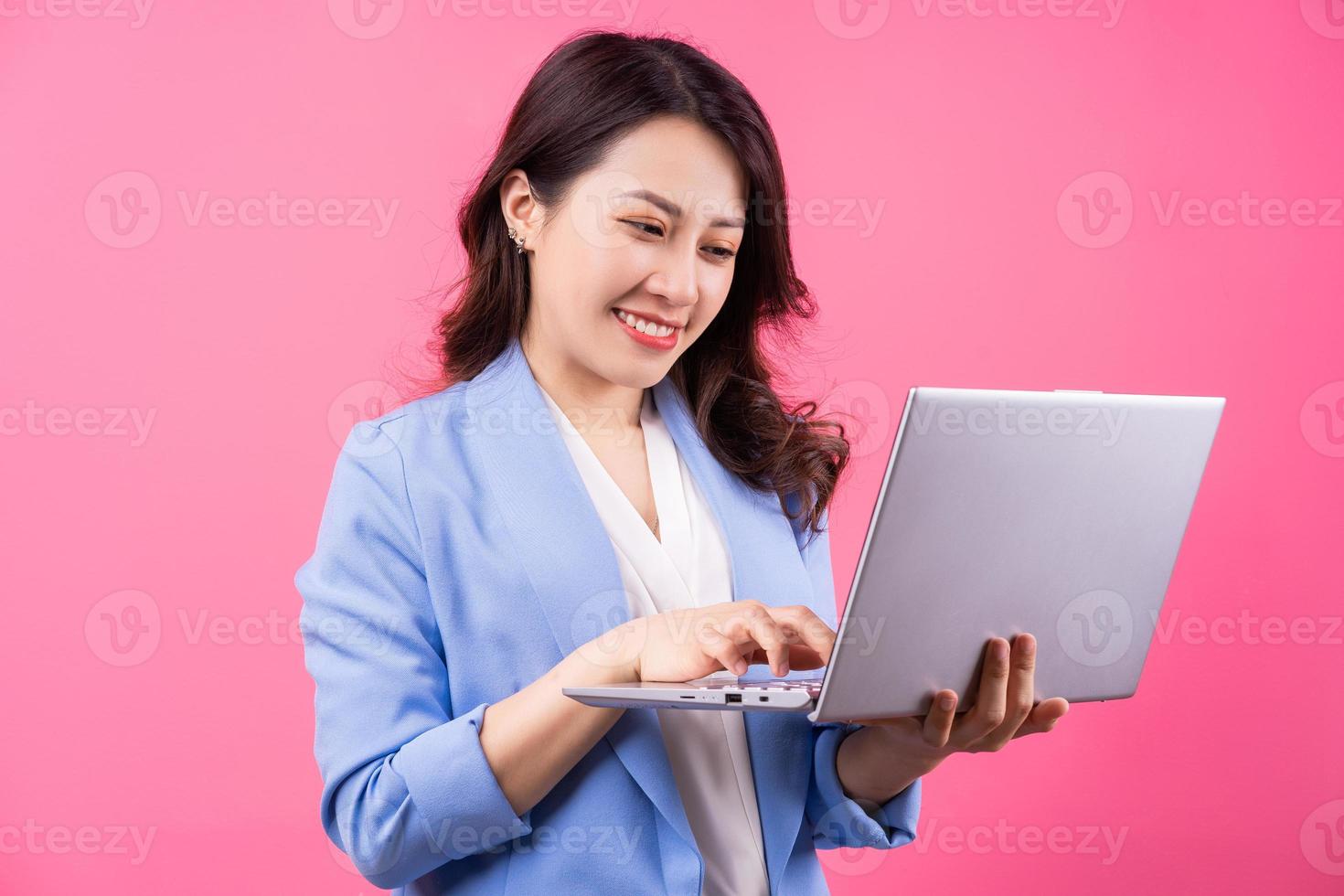 Mujer de negocios asiática sosteniendo portátil sobre fondo rosa foto