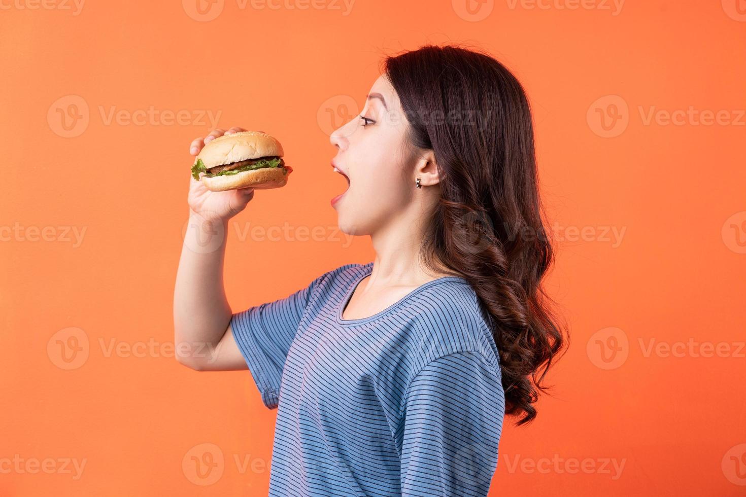 Joven mujer asiática comiendo hamburguesas sobre fondo naranja foto