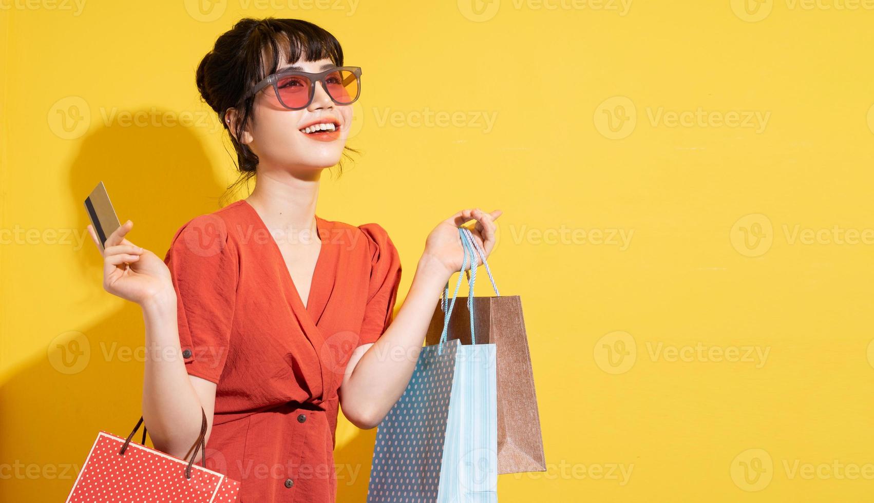 Joven empresaria asiática sosteniendo bolsas de la compra posando sobre fondo amarillo foto