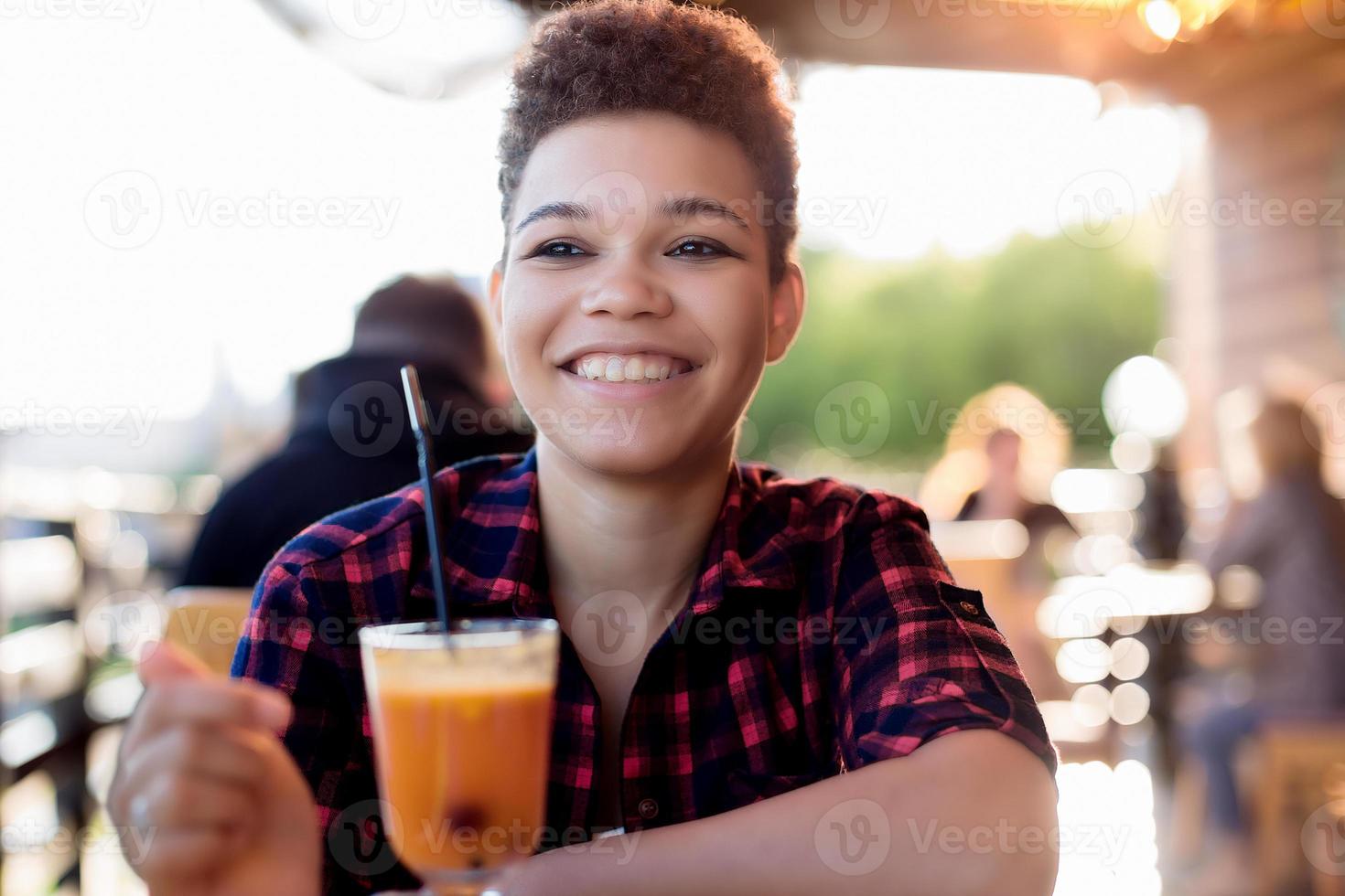 Hermosa mujer afroamericana con pelo corto en estaño un café de verano foto