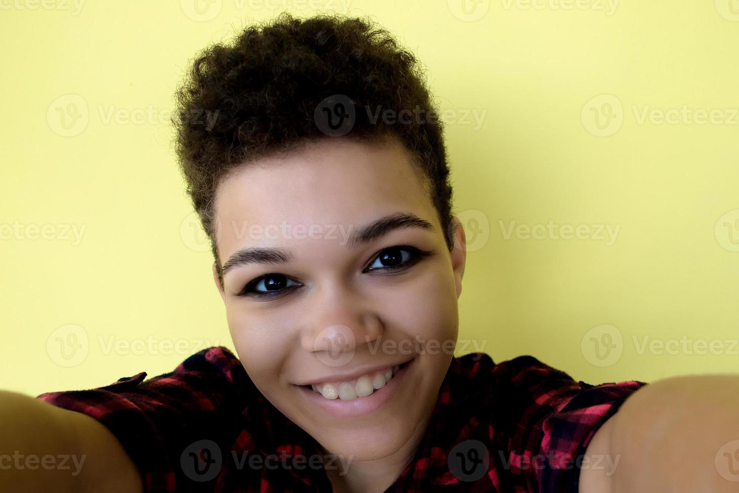 Beautiful and happy African American woman with short hair on a yellow background, takes a selfie, close-up portrait photo