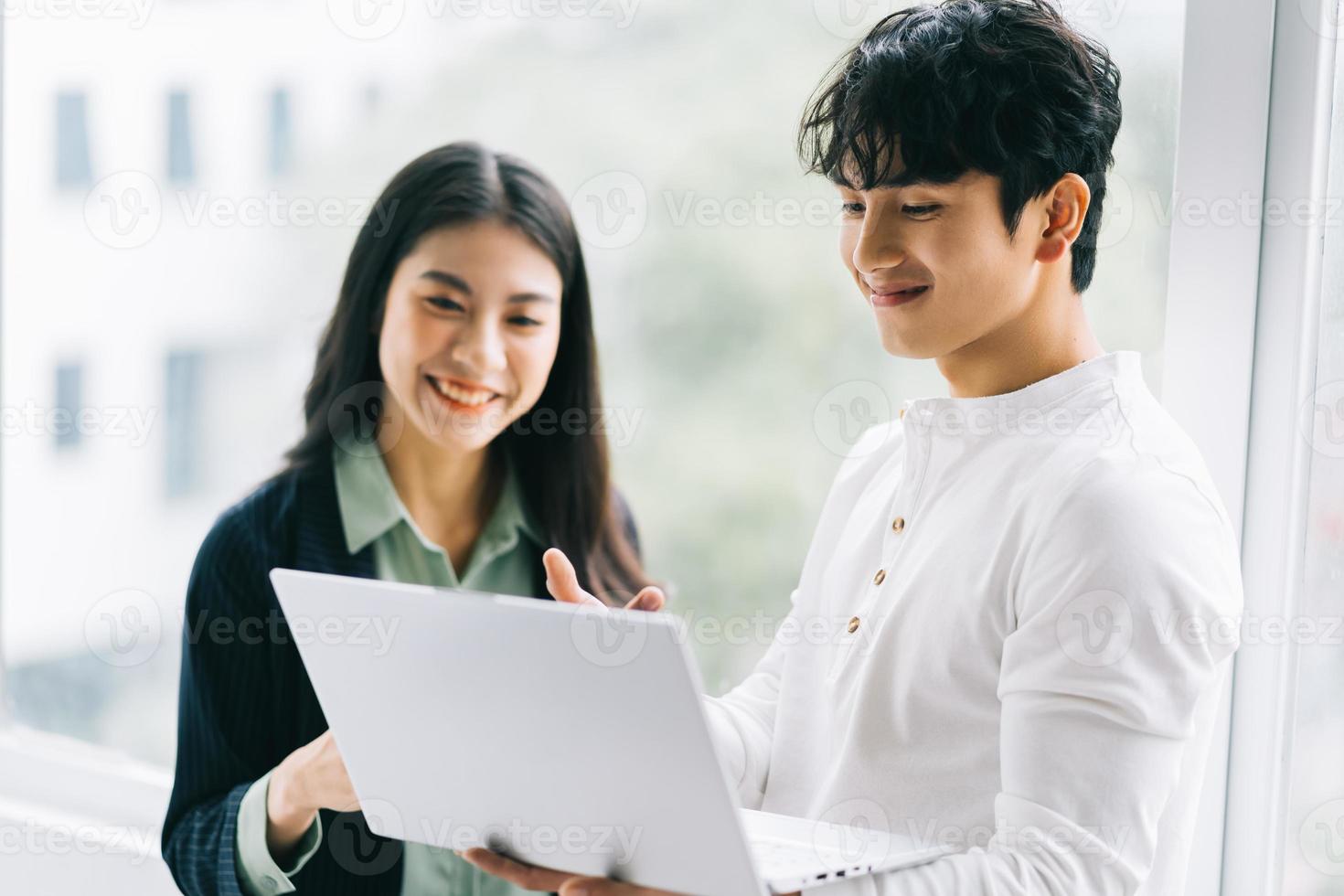 dos colegas asiáticos están discutiendo el trabajo. el empresario sostiene una computadora portátil en la mano foto