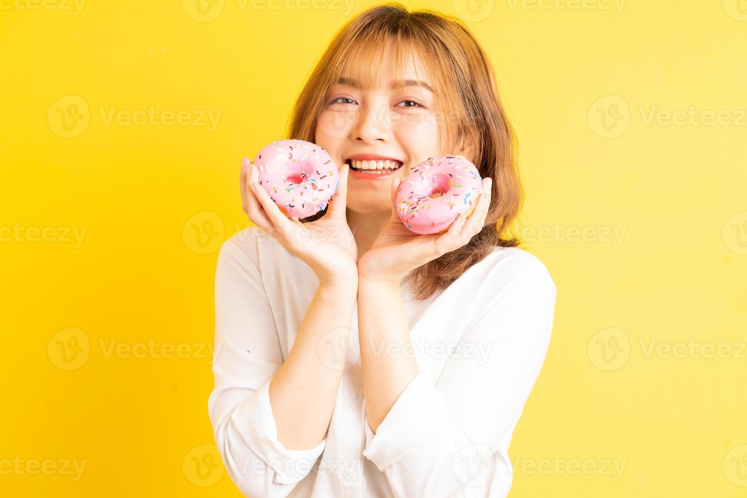 Joven asiática sosteniendo donut con expresión alegre en el fondo foto