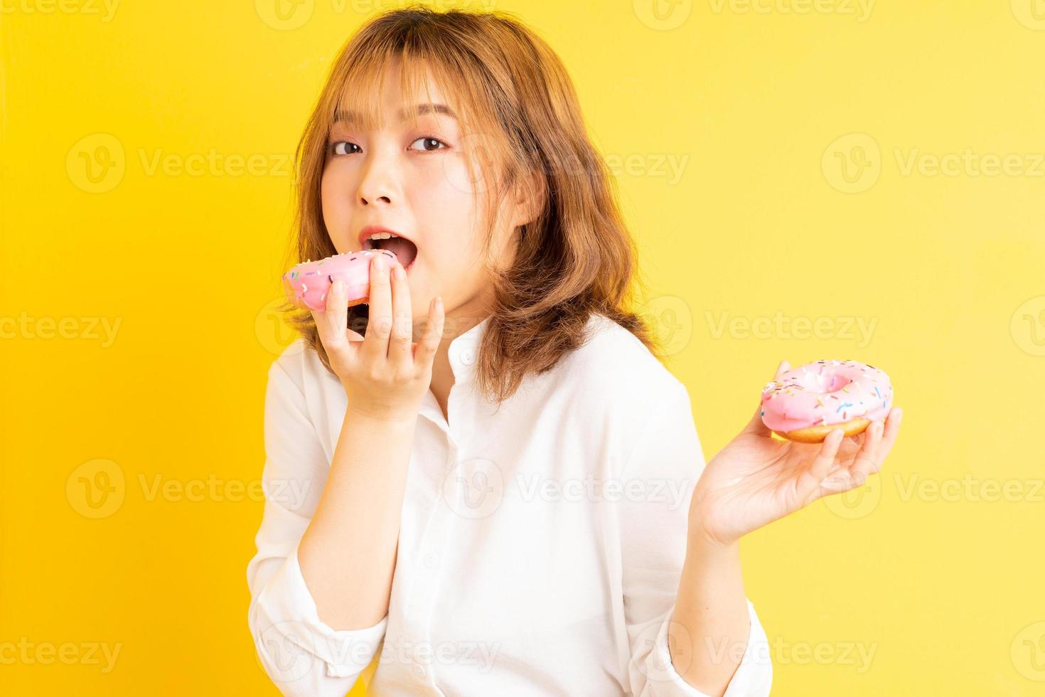 Joven asiática sosteniendo donut con expresión alegre en el fondo foto