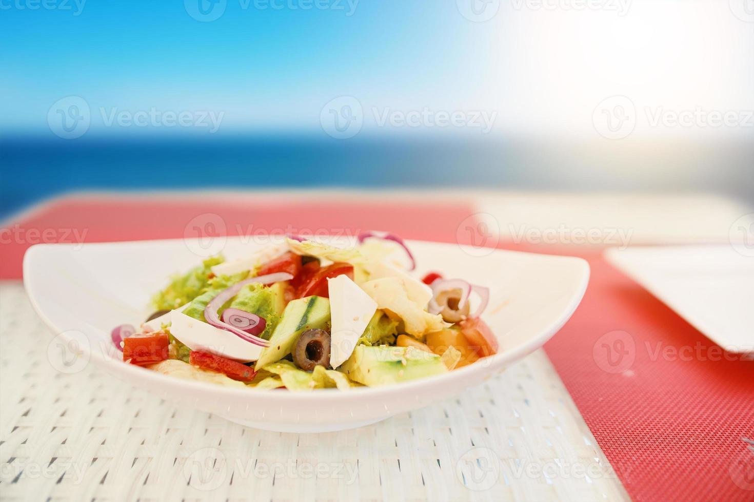 Ensalada vegetariana en plato de cerámica sobre mesa de rafia blanca. foto