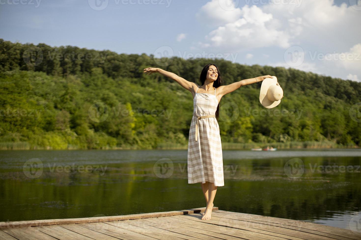 Relaxing young woman standing on wooden pier at the lake photo