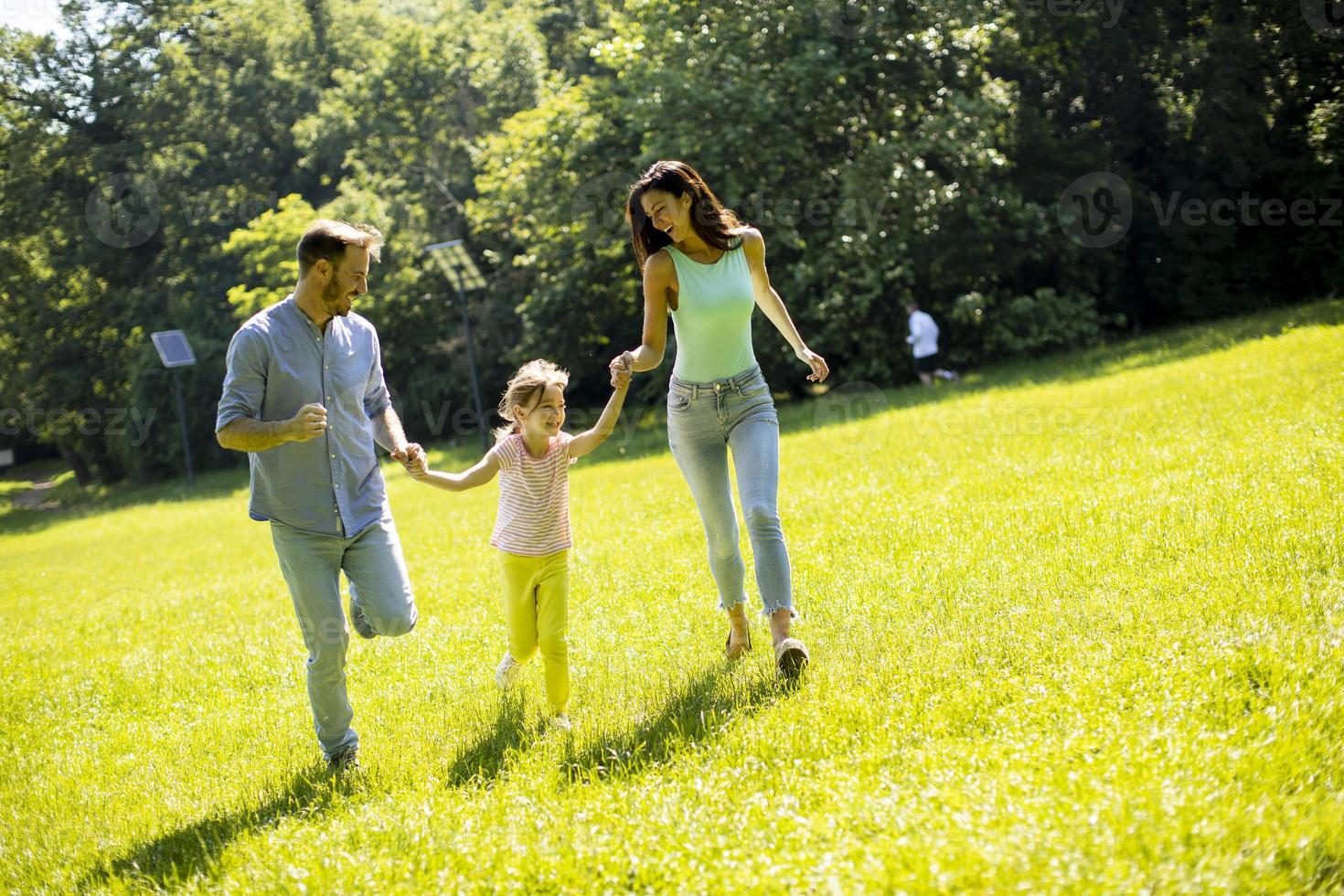 Happy young family with cute little daughter running in the park on a sunny day photo