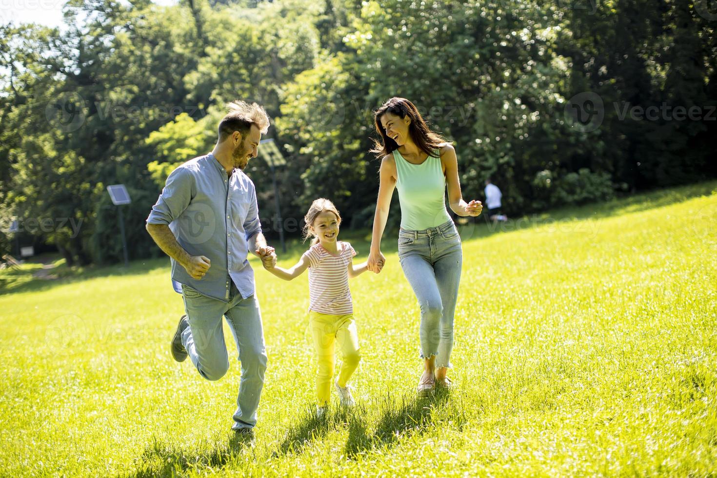 Happy young family with cute little daughter running in the park on a sunny day photo