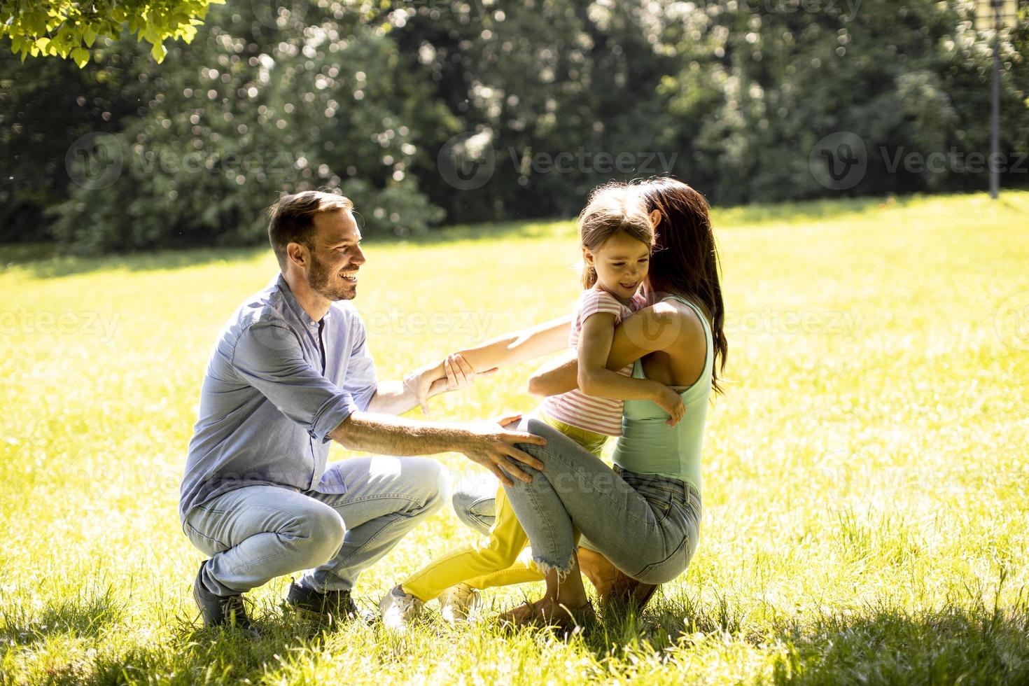 Familia joven feliz con linda hijita divirtiéndose en el parque en un día soleado foto