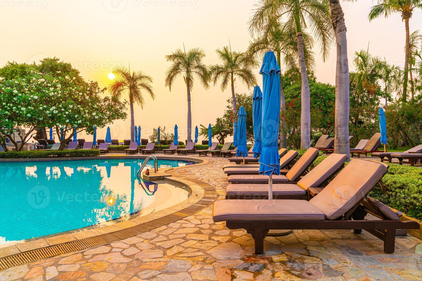 Beach chairs or pool beds with umbrellas around swimming pool at sunset time photo