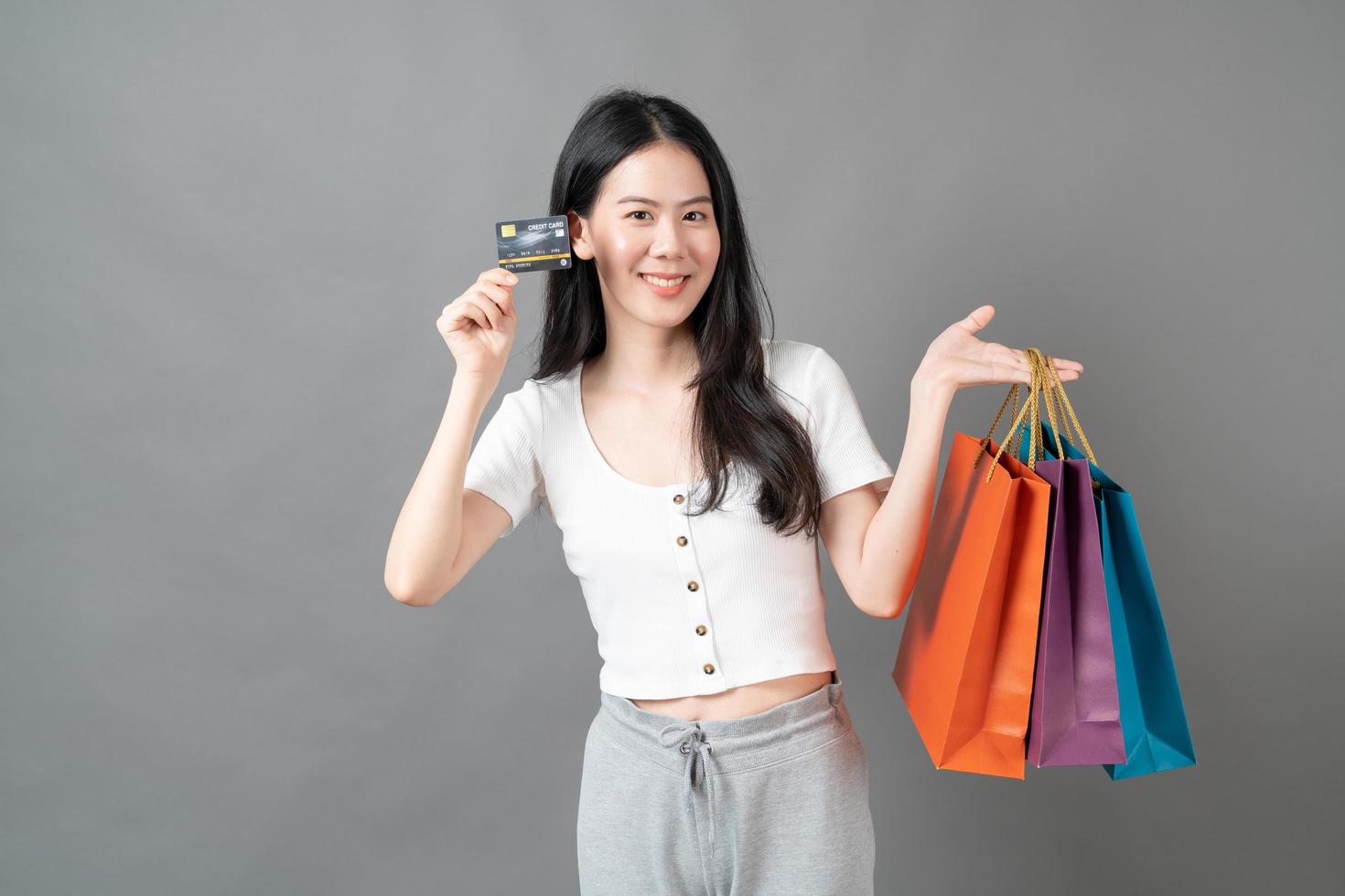 Joven mujer asiática mano sujetando una bolsa de compras y una tarjeta de crédito sobre fondo gris foto