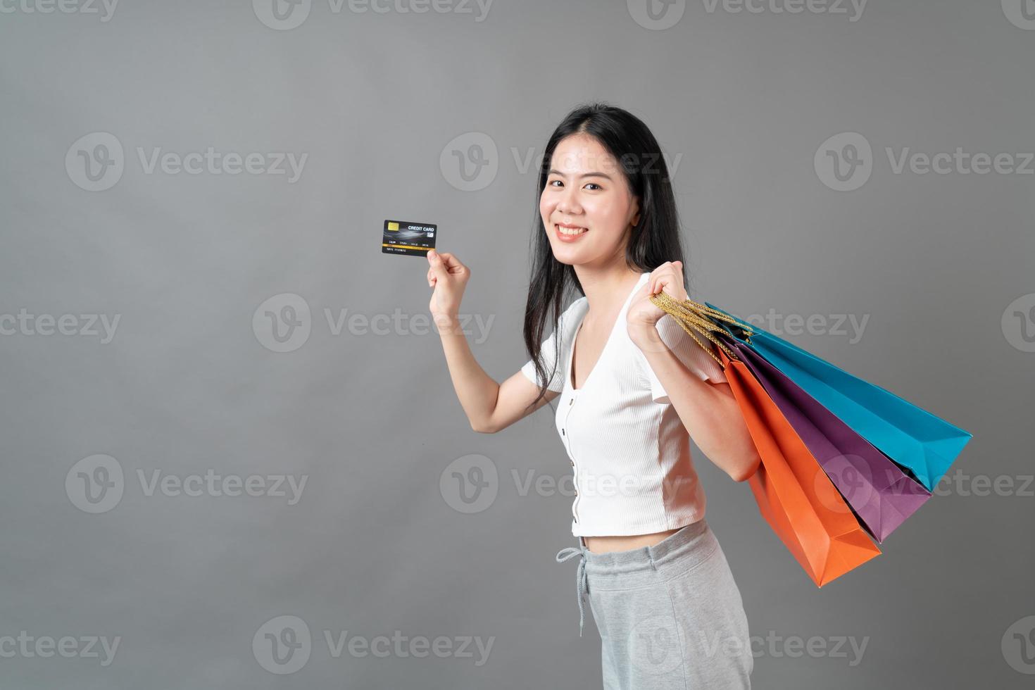 Joven mujer asiática mano sujetando una bolsa de compras y una tarjeta de crédito sobre fondo gris foto