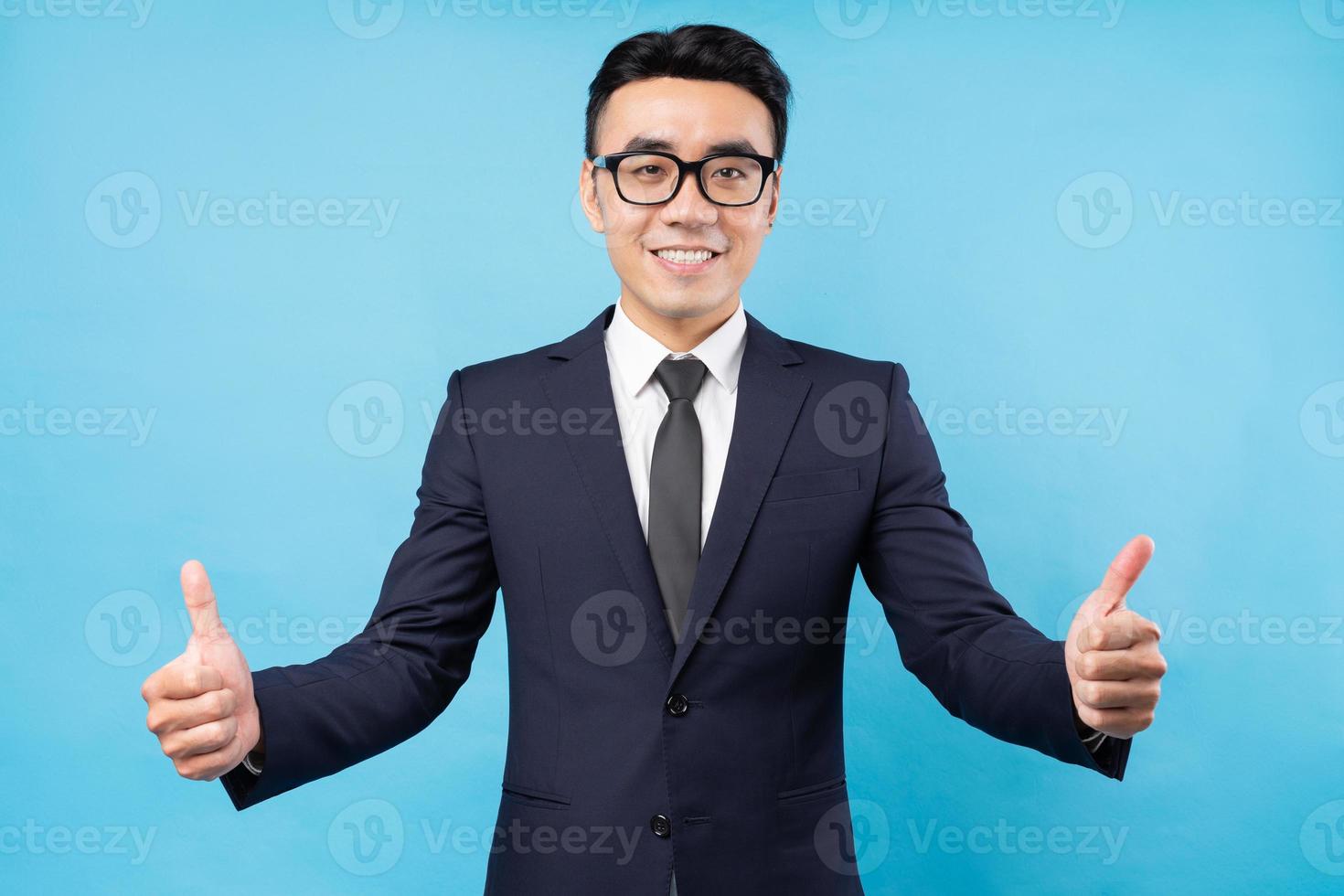 Empresario asiático dando pulgares hacia arriba sobre fondo azul. foto