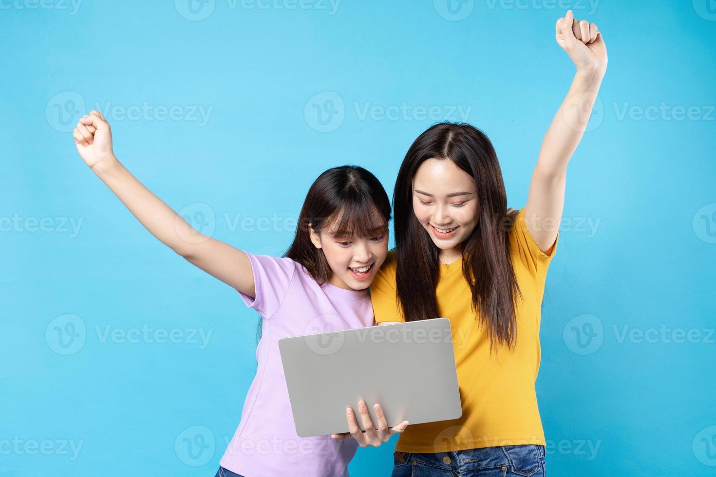 Two beautiful young Asian girls using laptop on blue background photo