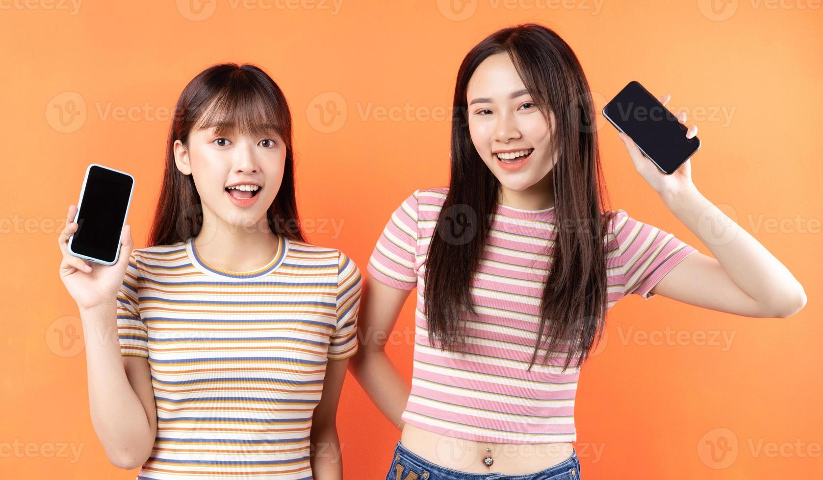 Two beautiful young Asian girls using mobile phones on orange background photo
