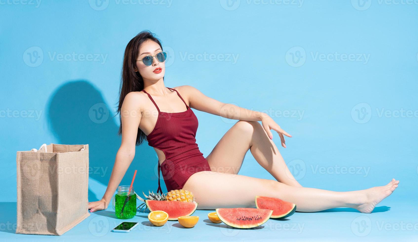 Mujer asiática en traje de baño rojo con frutas tropicales sobre fondo azul. foto