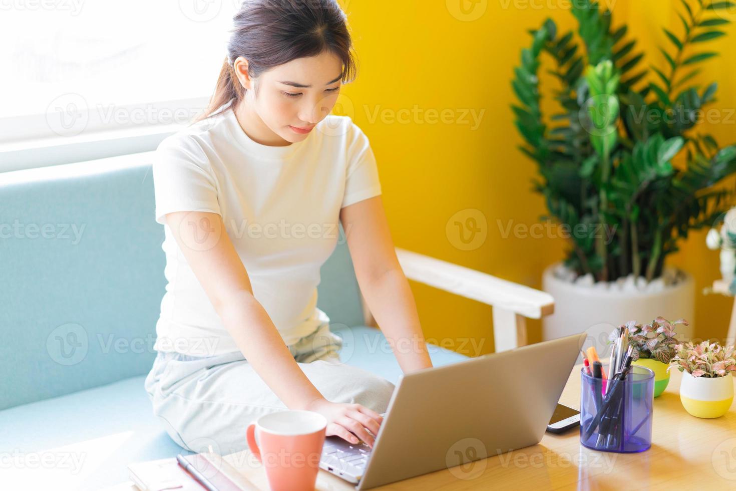 Joven mujer asiática sentada en un sofá trabajando en casa foto