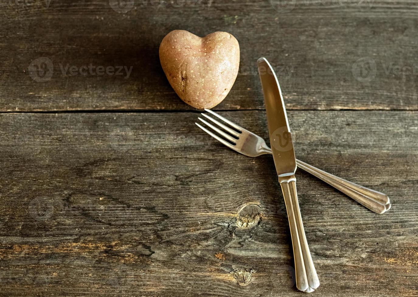 Red potatoes in the shape of a heart on a wooden background with a fork and knife. The concept of agriculture, harvesting, vegetarianism. Valentine's Day. square, ugly food. photo