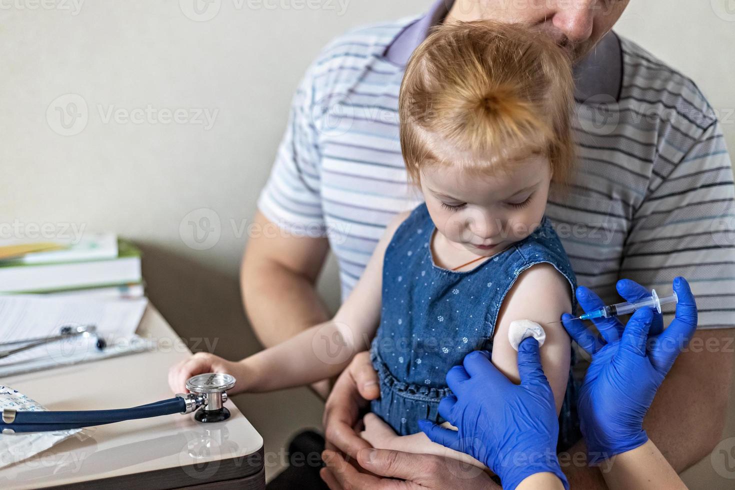 A little girl with her father in the doctor's office at the clinic is being vaccinated against the coronavirus.The concept of vaccination, immunization, prevention against Covid-19. photo