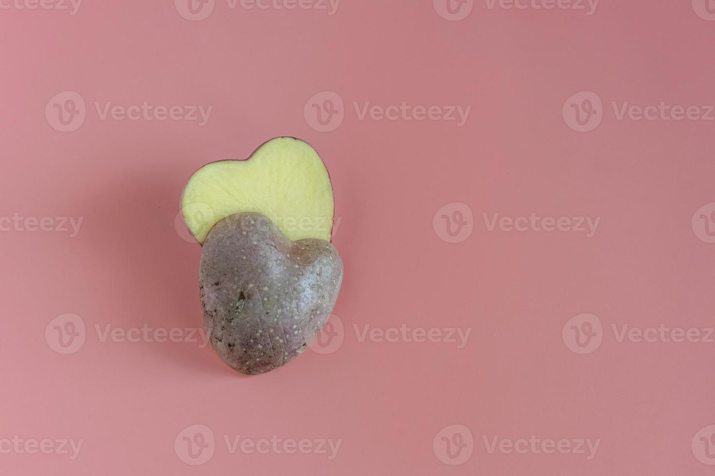 Heart shaped potatoes cut in half on a pink background. Concept of farming, harvesting, vegetarianism photo