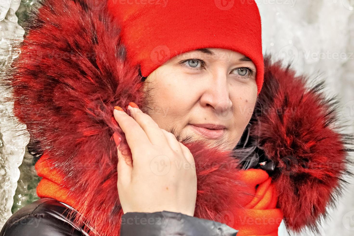 Portrait of a woman in a red hat and scarf, warm jacket against the background of an ice wall. Winter photo